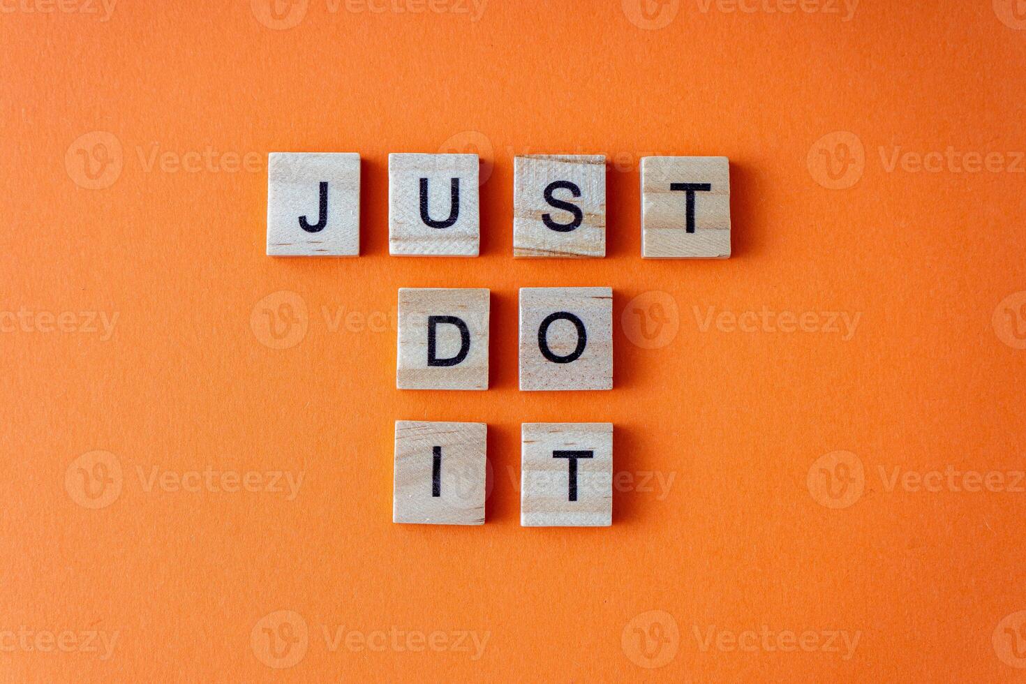 Just do it word. The phrase is laid out in wooden letters top view. Motivation. Orange flat lay background. photo