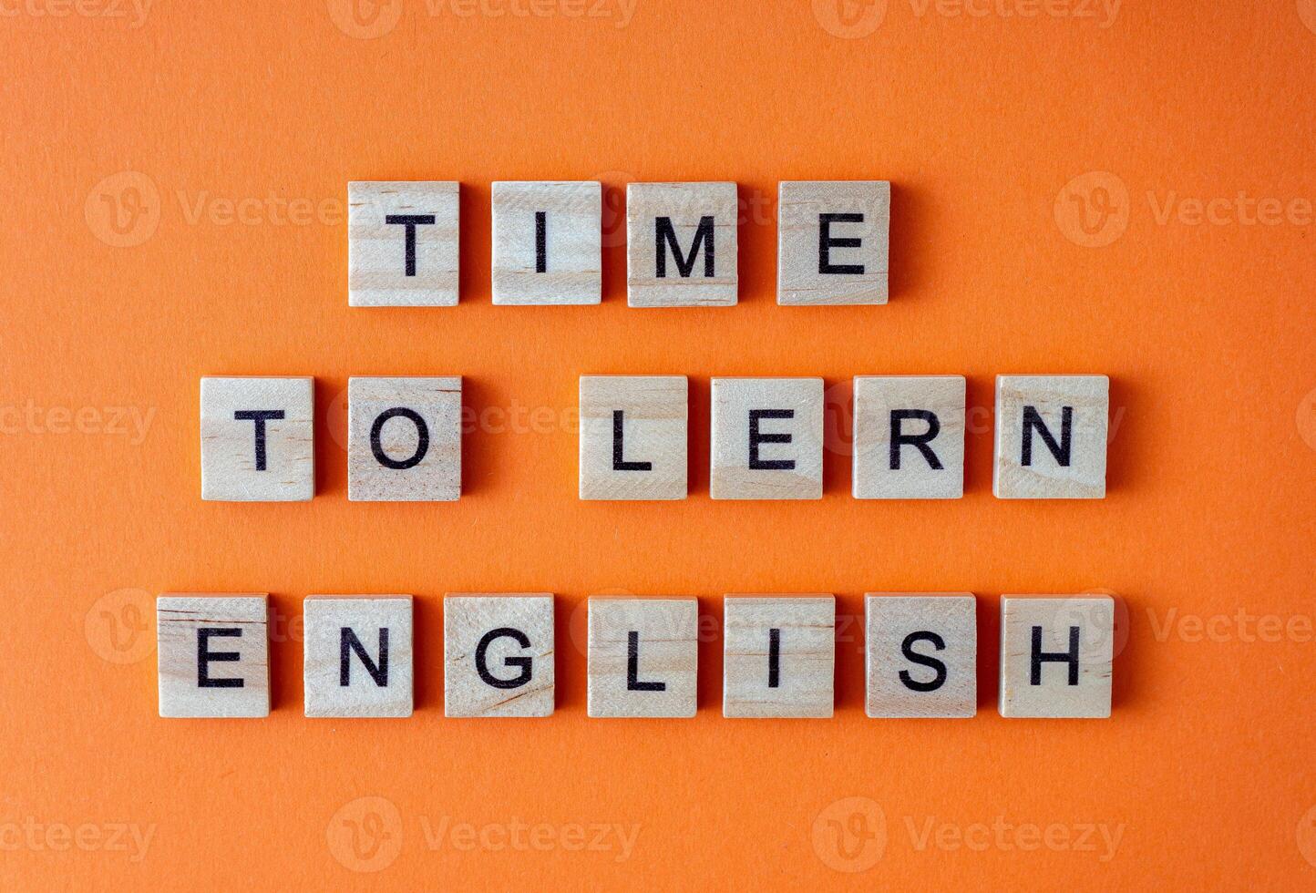 Word time to learn English. Motivation. The phrase is laid out in wooden letters top view. Motivation. Orange flat lay background. photo