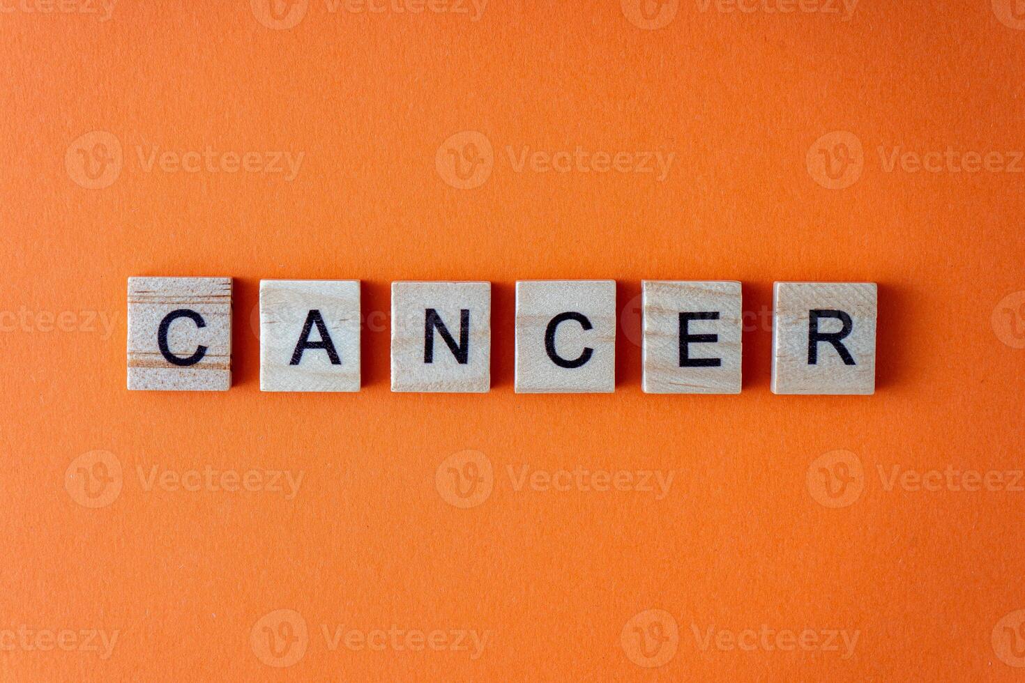 Cancer word . The phrase is laid out in wooden letters top view. Orange flat lay background. photo