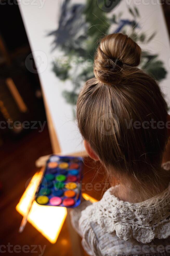 little cute girl draws with paints on canvas at the easel photo