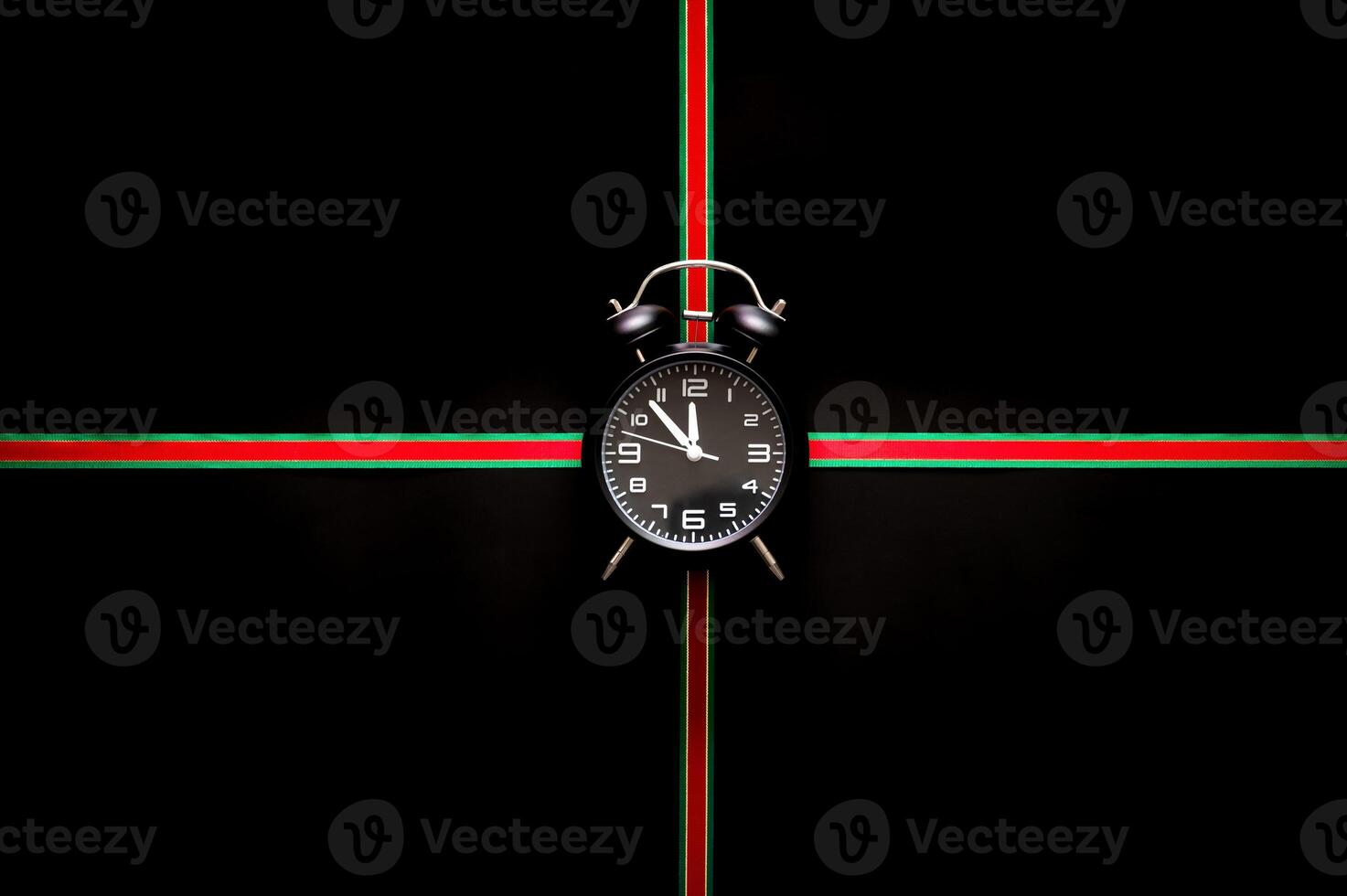 The alarm clock puts in the middle of green and red color ribbon on black background for Black Friday shopping day concept. photo