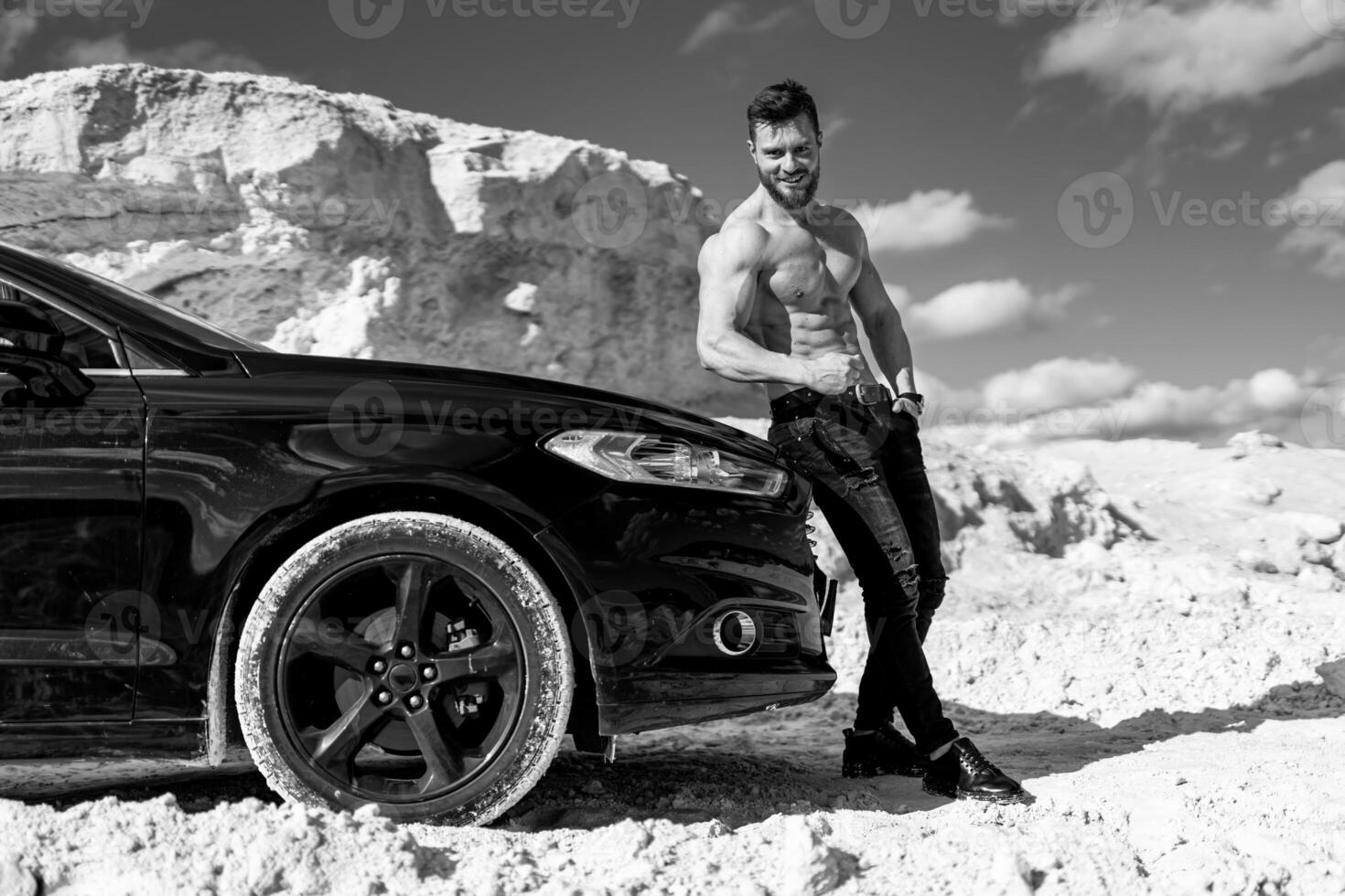 Brutal man with no shirt is standing on the road near car. Man in front of the luxury auto. Black and white photo. photo