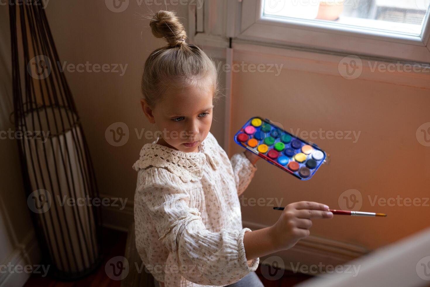 little cute girl draws with paints on canvas at the easel. the concept of early development of children's talents. photo