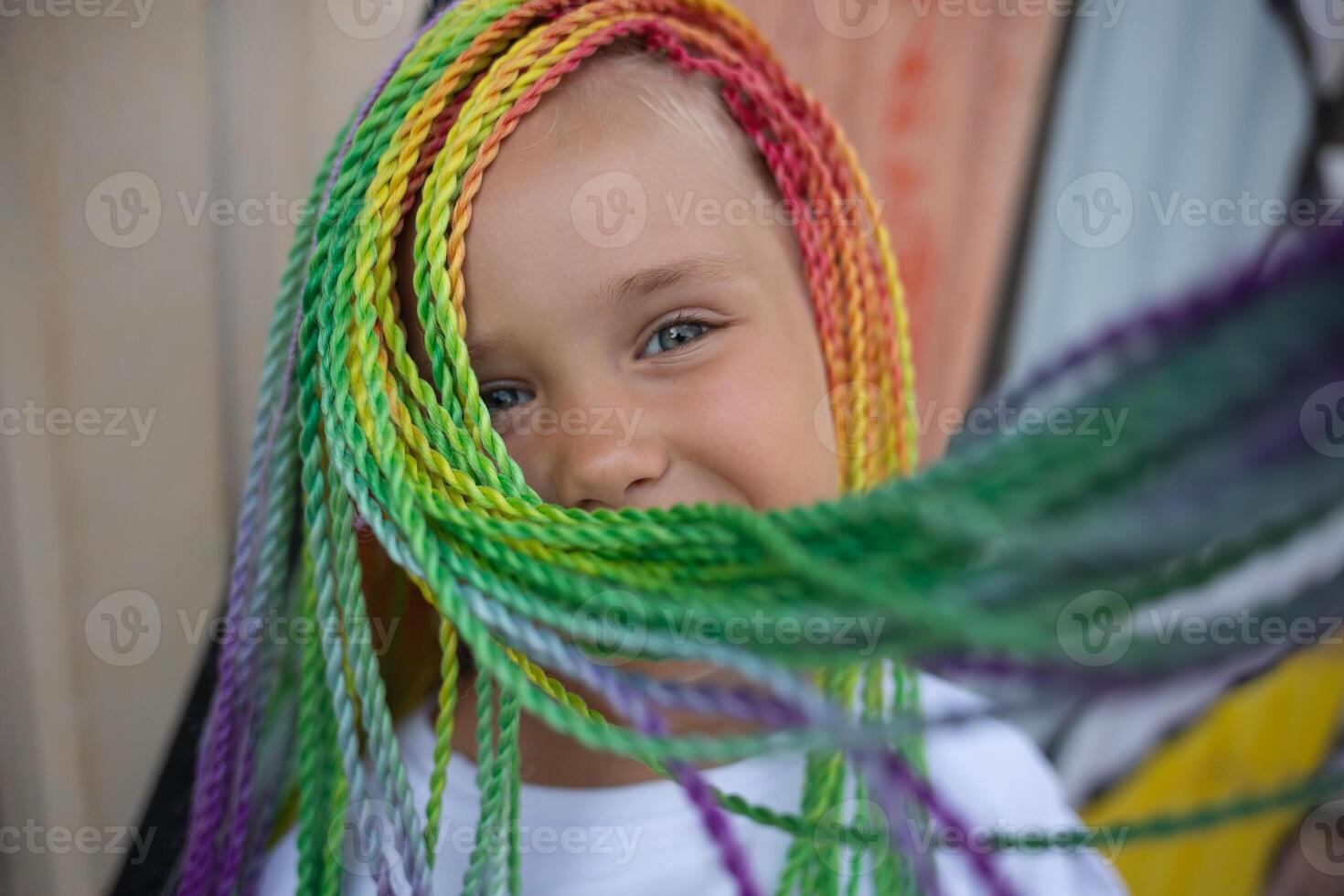 portrait of a little beautiful girl with multi-colored african braids on the background of a colorful wall photo