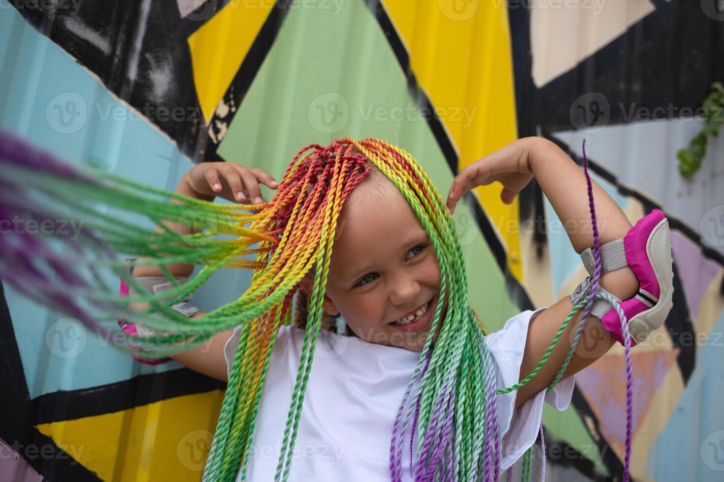 portrait of a little beautiful girl with multi-colored african braids on the background of a colorful wall photo