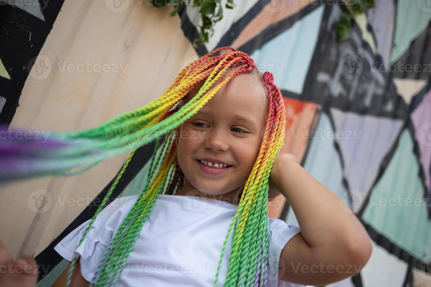 portrait of a little beautiful girl with multi-colored african braids on the background of a colorful wall photo