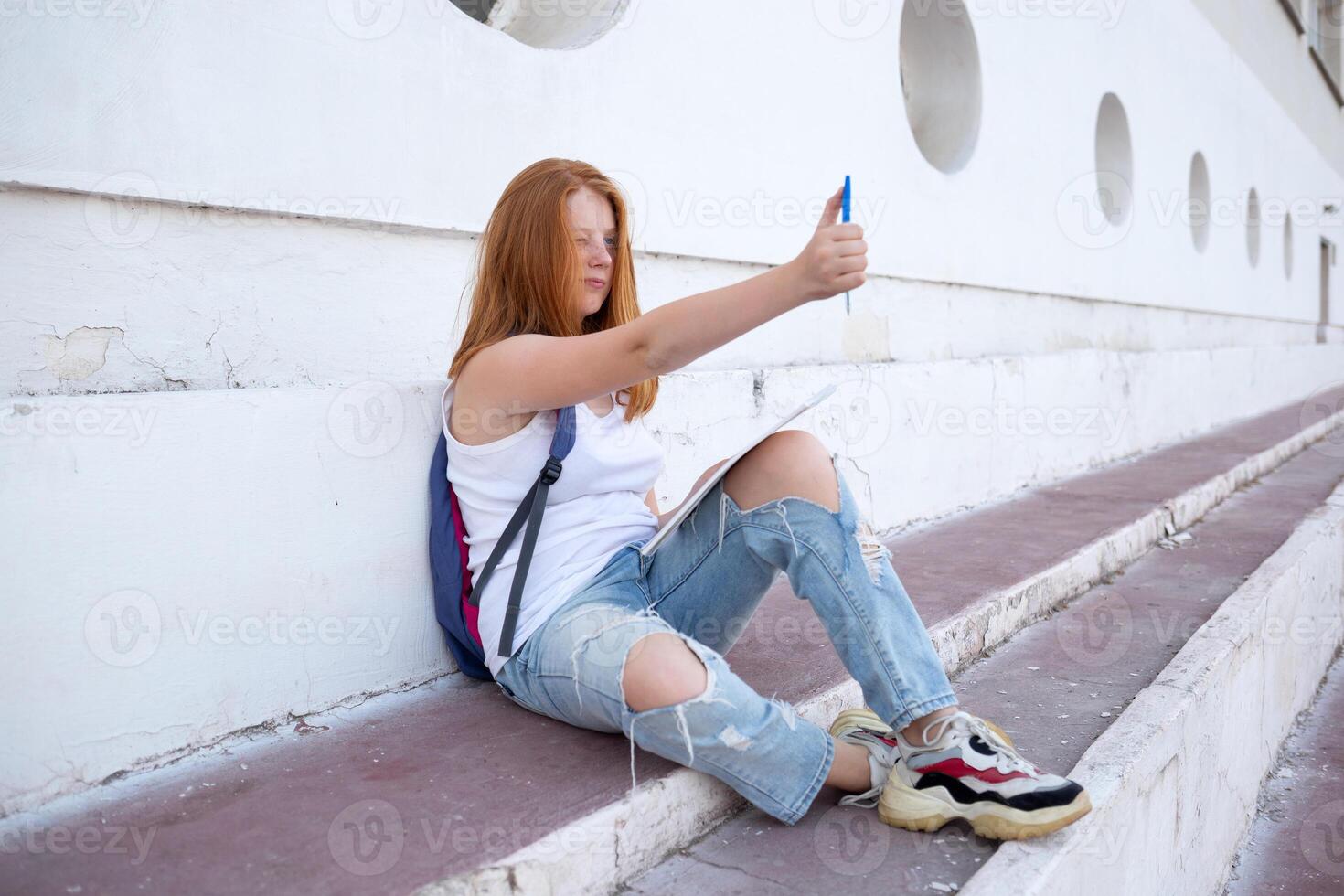 teenage girl draws in the sketchbook while sitting on the steps photo