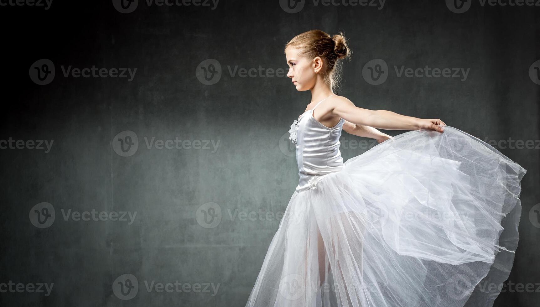 Ballerina. Cute little girl posing and dancing in studio. The girl is studying ballet. Dark background. photo