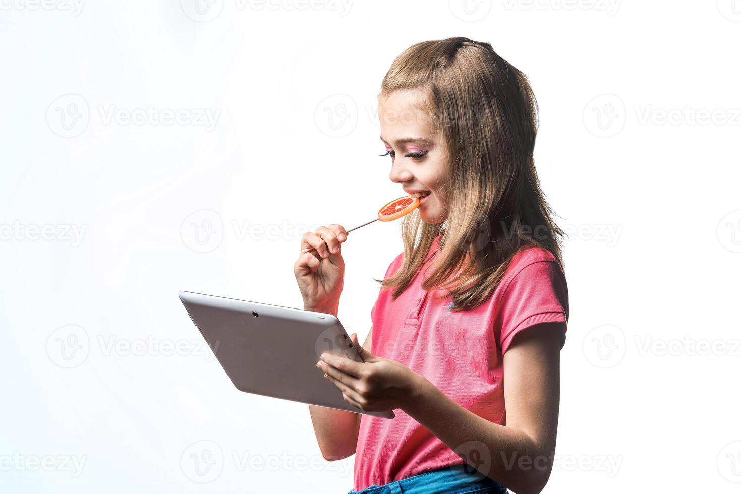 Little girl with a tablet computer and candy on a white background. Emotions of the child. photo