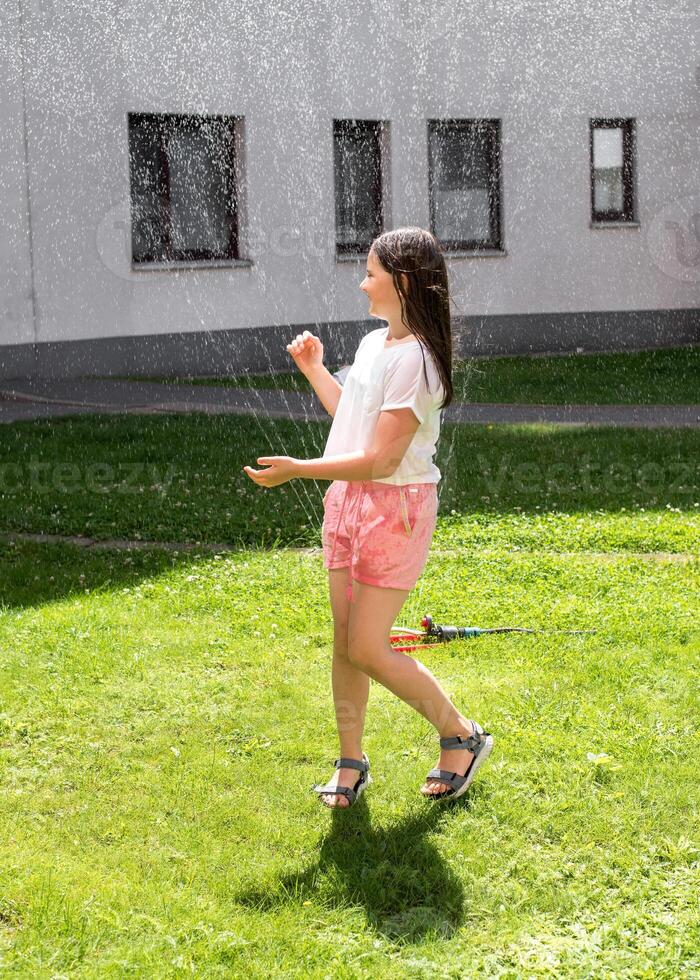 A girl jumps under a sprinkler on a hot summer day photo