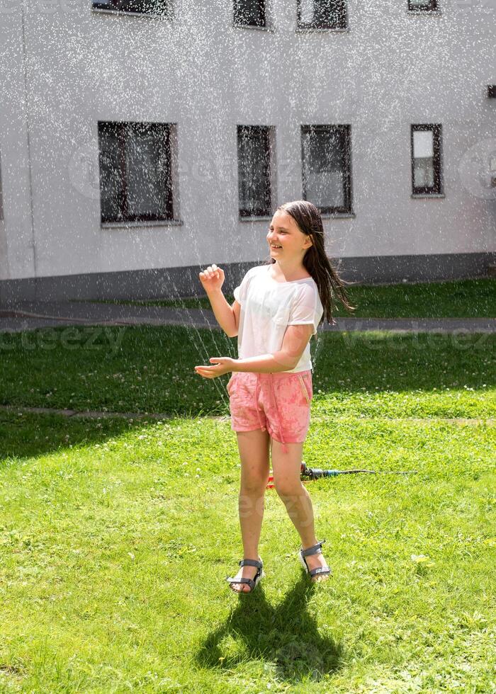 A girl jumps under a sprinkler on a hot summer day photo