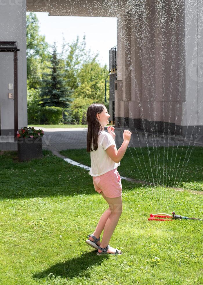 A girl jumps under a sprinkler on a hot summer day photo