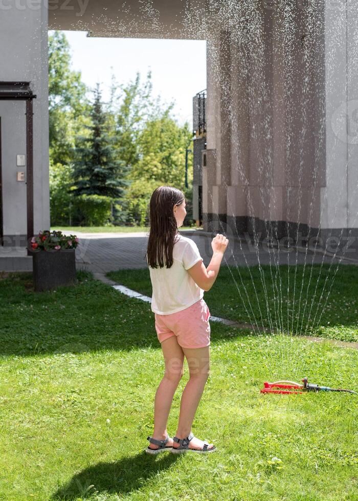 A girl jumps under a sprinkler on a hot summer day photo
