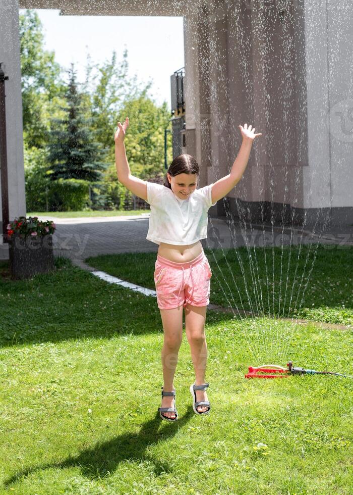 A girl jumps under a sprinkler on a hot summer day photo