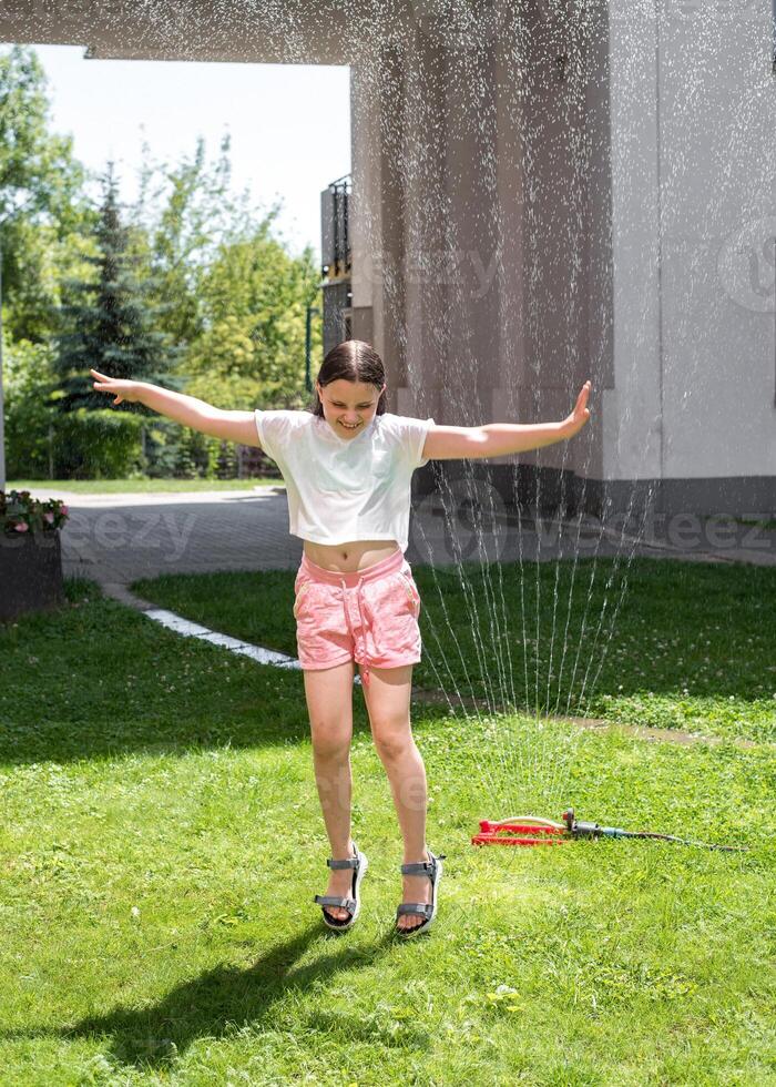 A girl jumps under a sprinkler on a hot summer day photo