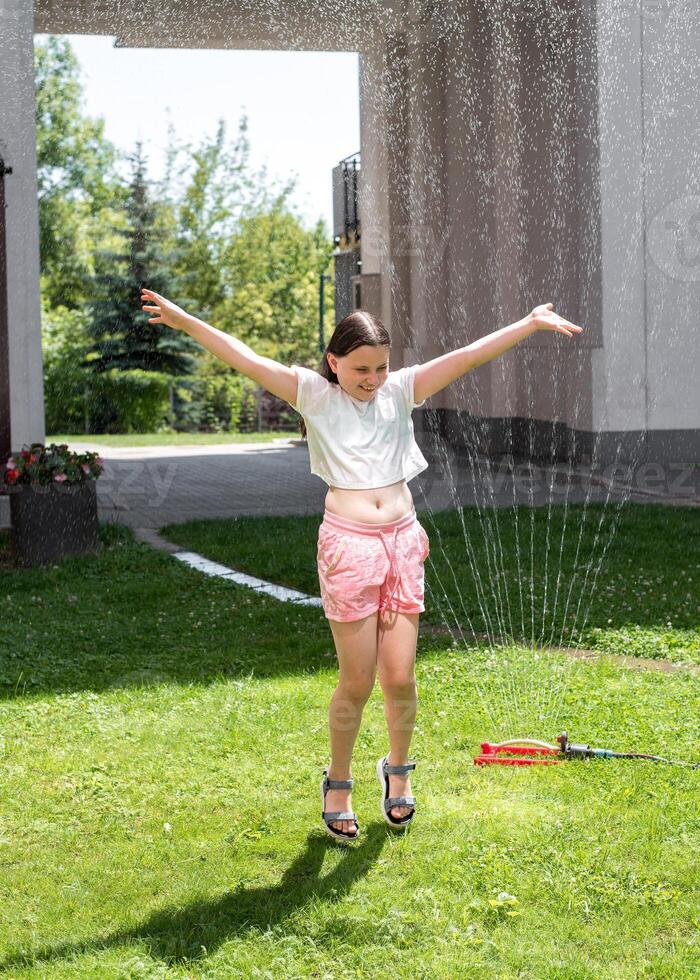 A girl jumps under a sprinkler on a hot summer day photo