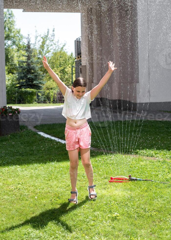 A girl jumps under a sprinkler on a hot summer day photo