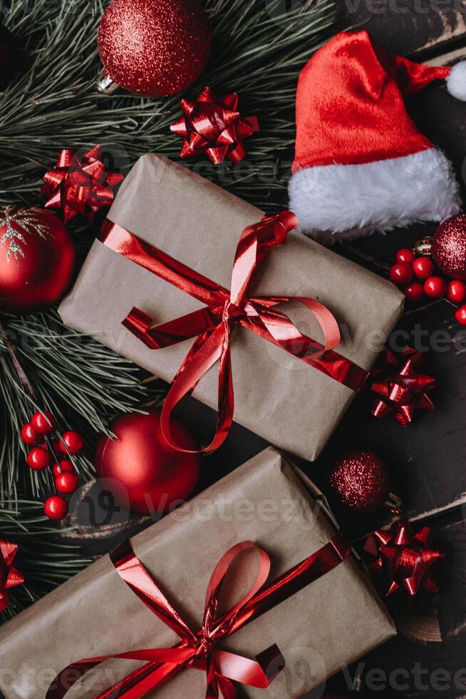 Top view photo Christmass flatlay gift boxes,red christmas tree toys,Santa hat and spruce brance on wooden background. Xmas backdrop with space for text.Copyspace.Close up.Vertical photo.