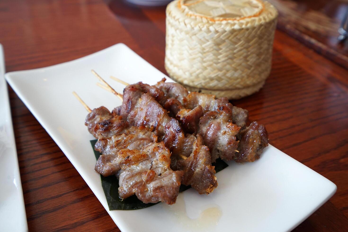 Close up Barbecue pork skewers served with wooden basket of sticky rice, Thai recipe photo