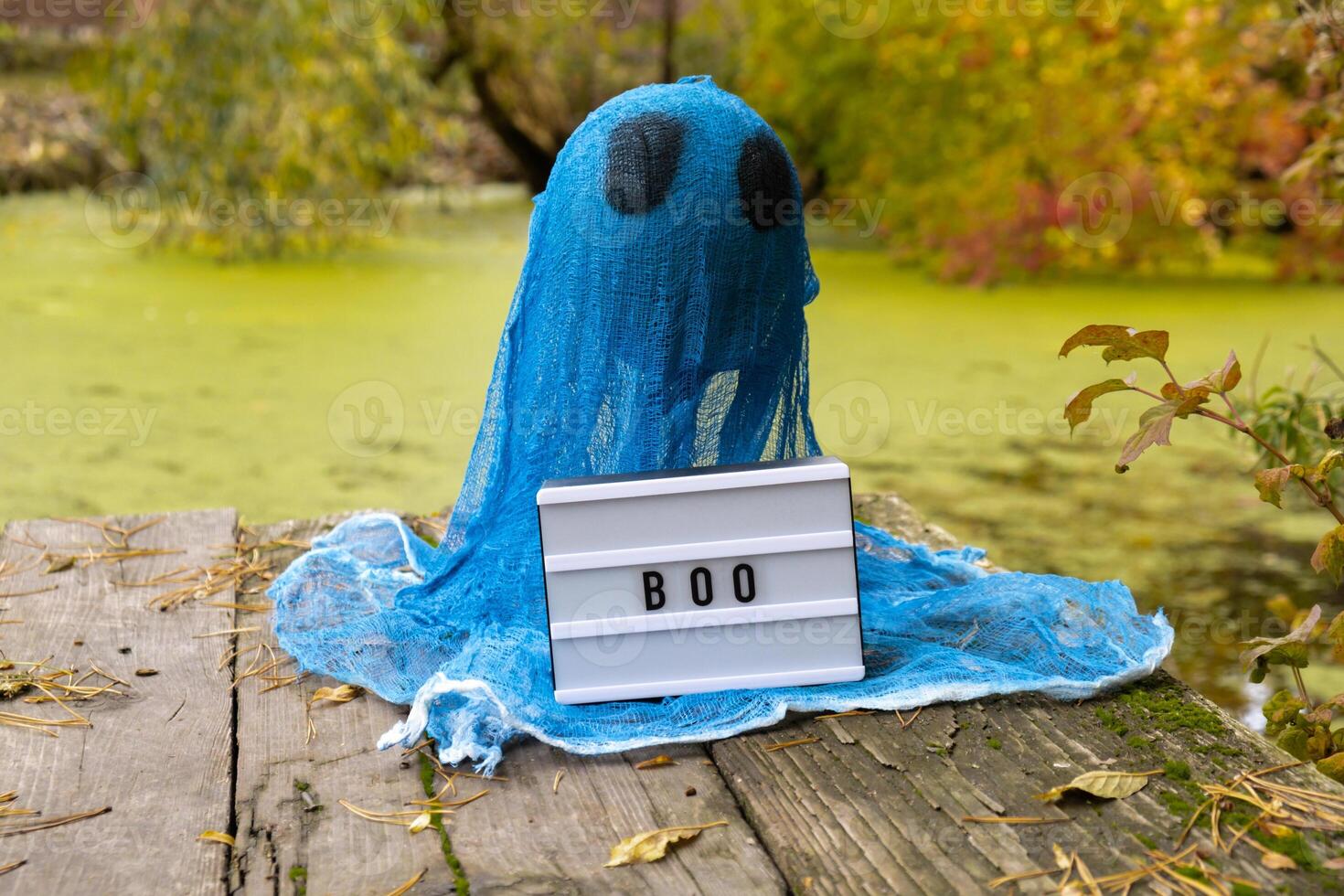 Creative handmade Halloween holiday decoration. blue ghost with Lightbox BOO text in autumn leaves forest. Zero waste homemade decor. Mystic place supernatural photo