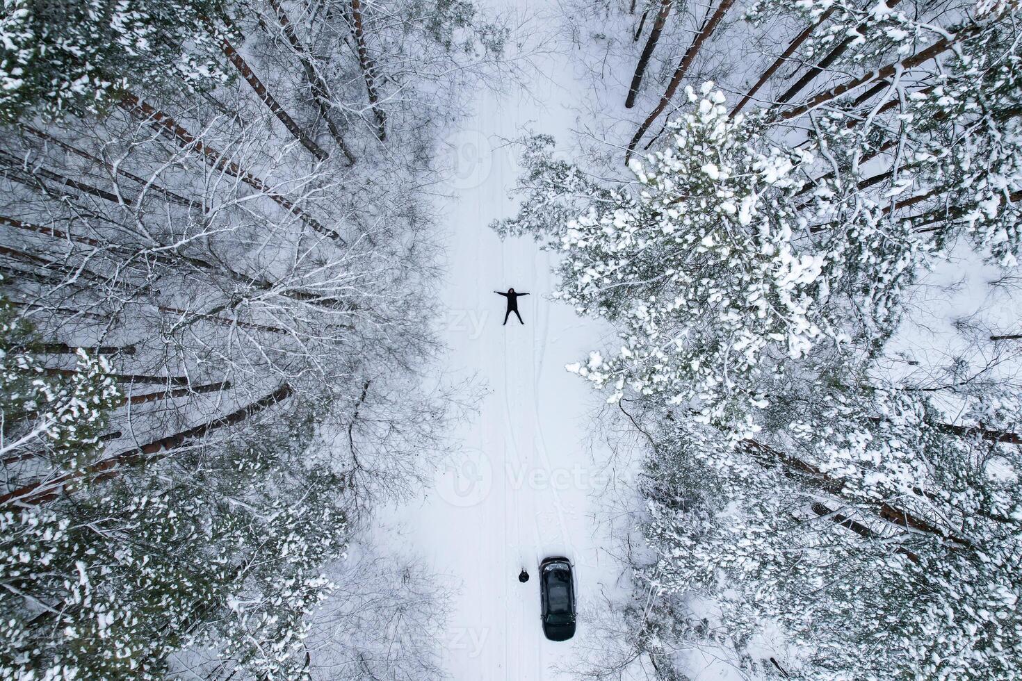 Man lying down making snow angel, top view. Aerial view beautiful snowy winter forest. Road in snow wintertime. Frosty morning travel concept background. Amazing winter scene. Christmas theme. Spruce covered with snow photo