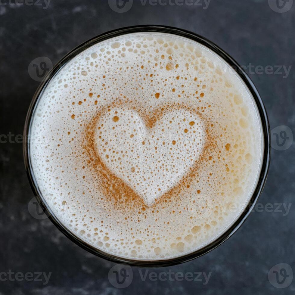 Heart-shaped foam atop a beer in a glass on a dark grey surface photo