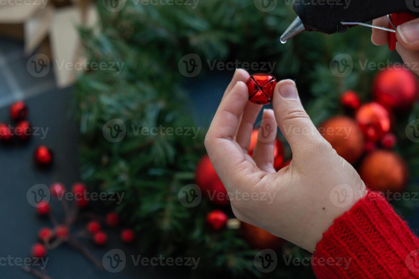 Crafter using hot glue Step by step instruction of making handmade Christmas wreath made of festive decorations in red color. Female hands creating craft homemade decor. New year celebration. Winter holidays Step 2 photo