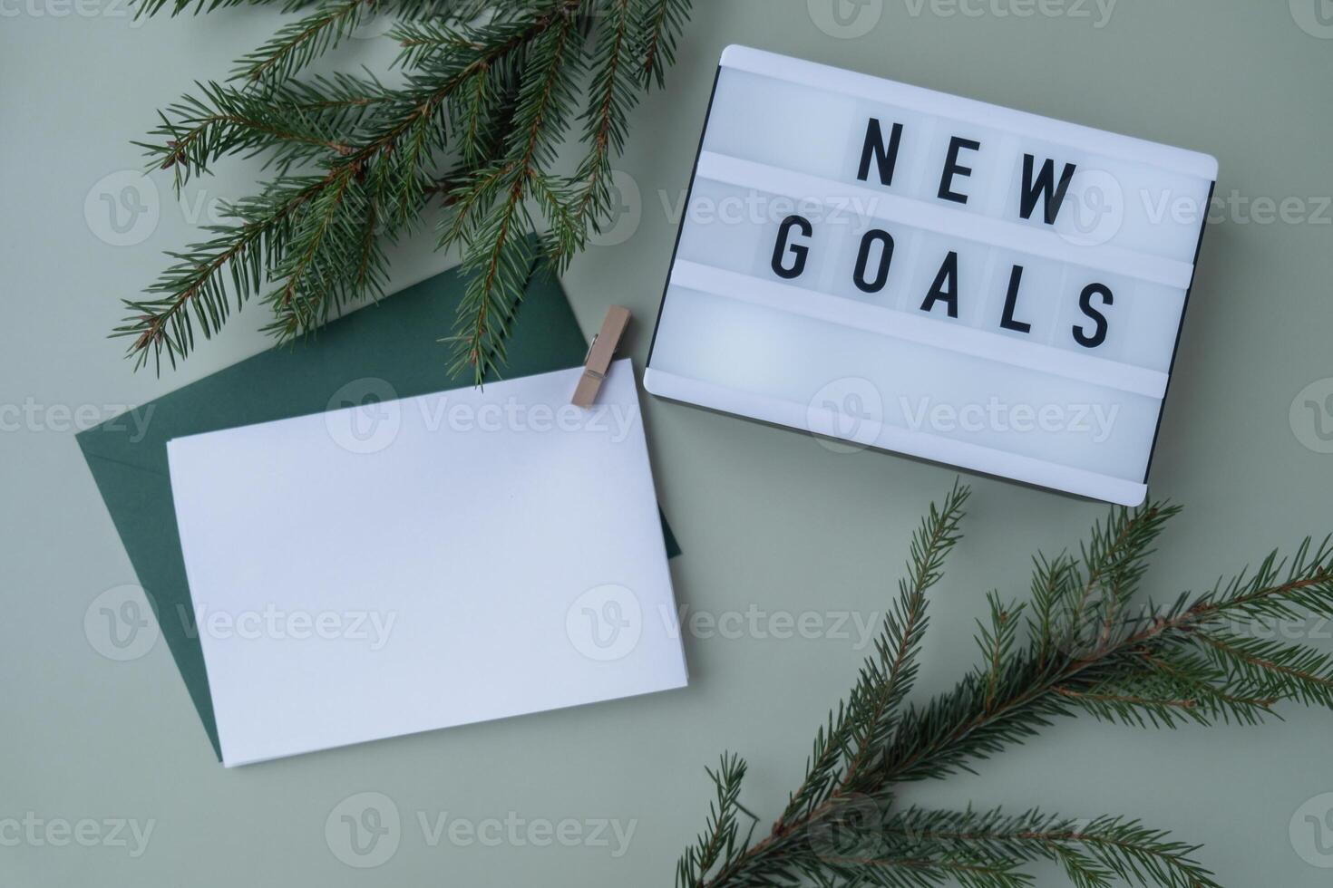 NEW GOALS text on Lightbox on green background with Christmas decor and copy space template mock up white envelope. New year aims resolutions. Planning and setting goals concept photo