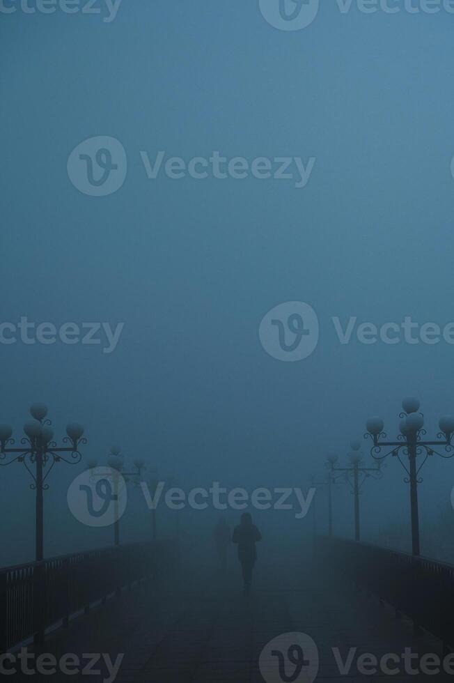 mystical silhouettes of people on a foggy bridge in the evening in autumn in fog mist photo