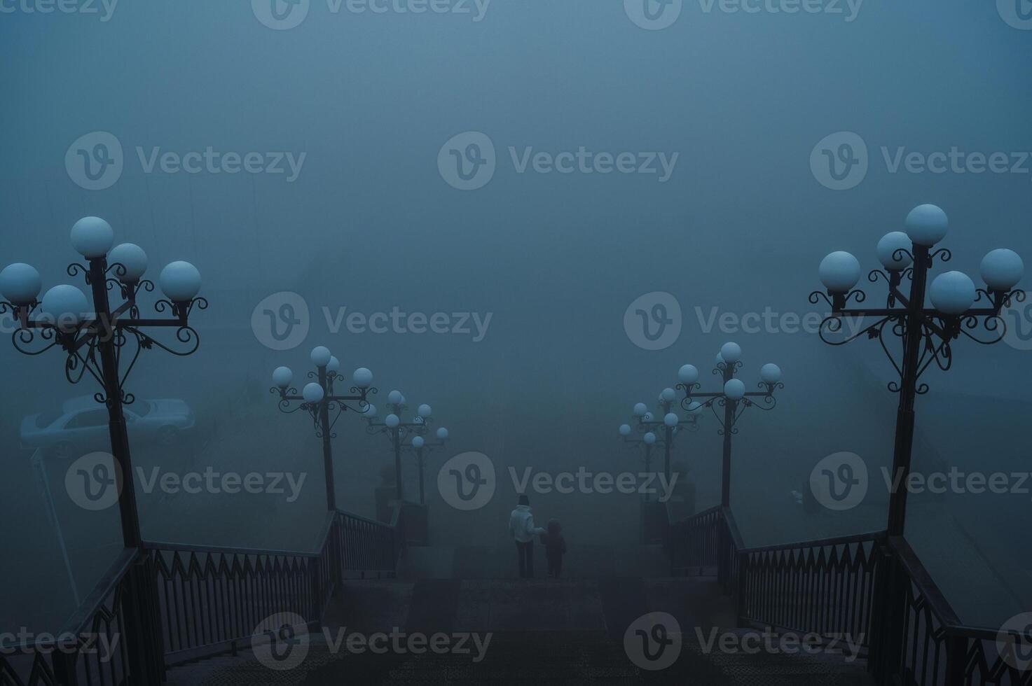 backs of a woman with a child boy going down the stairs on a foggy bridge in the city on an autumn morning in fog mist photo