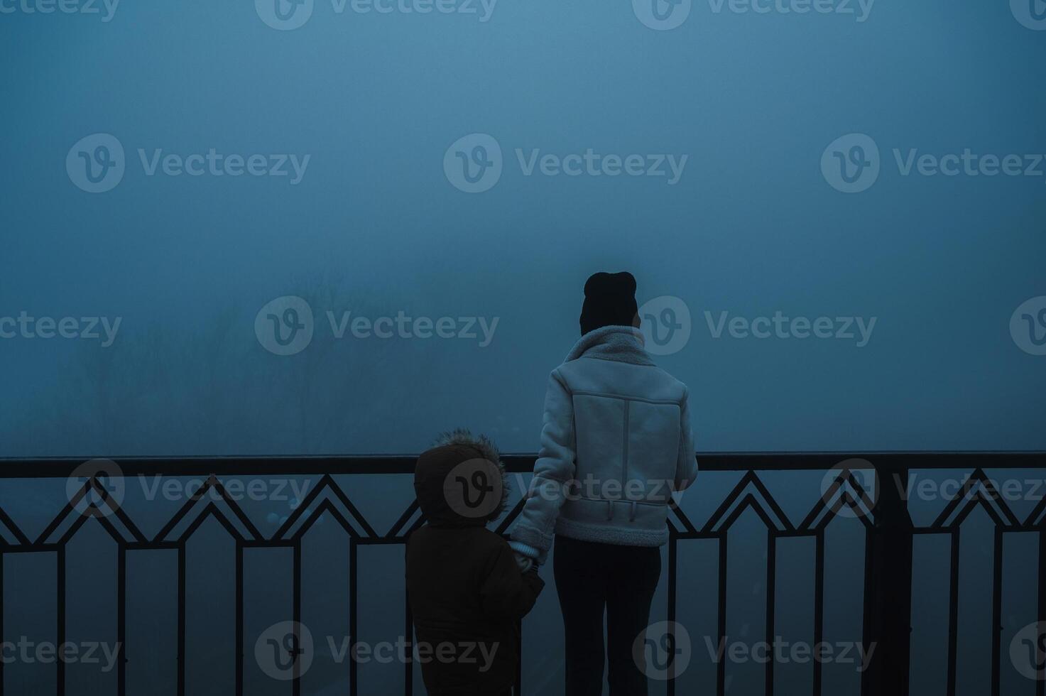 Backs of a woman with a child boy on a misty foggy bridge on an autumn evening in fog mist photo