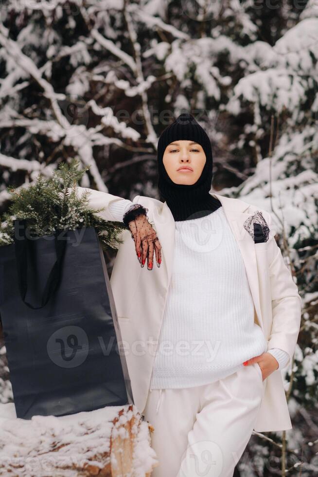 A girl in a white suit and balaclava with a package of Christmas trees in the winter forest on New Year's Eve.New Year's concept photo