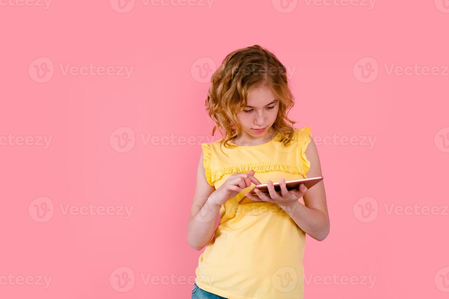 A teenage girl does her homework on a tablet. The student works and communicates with friends. Pink background with free space photo
