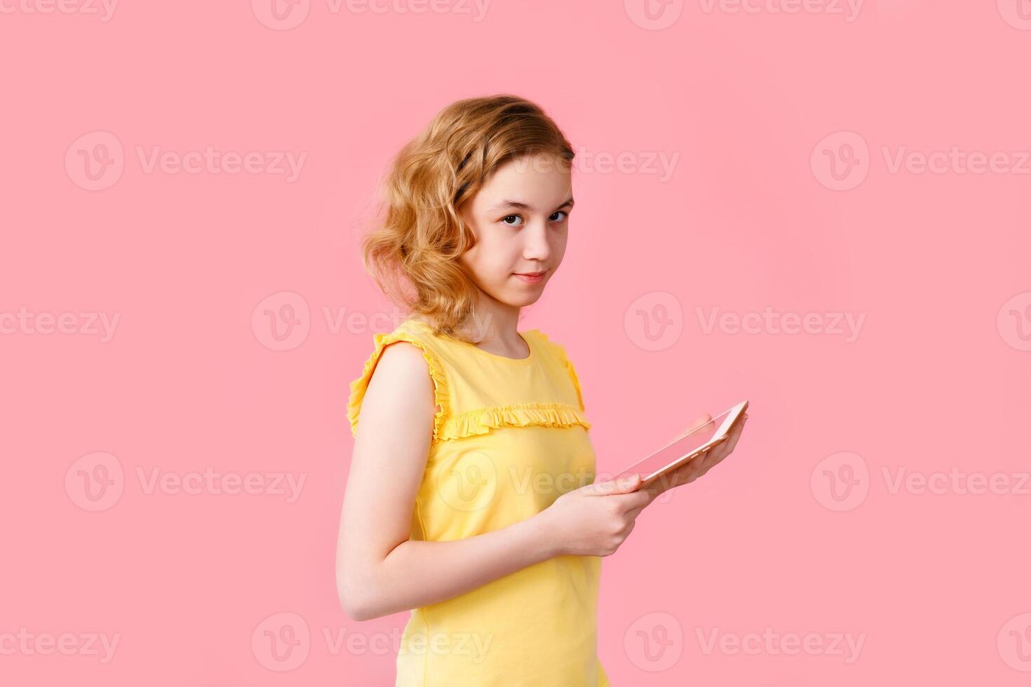 A teenage girl does her homework on a tablet. The student works and communicates with friends. Pink background with free space photo