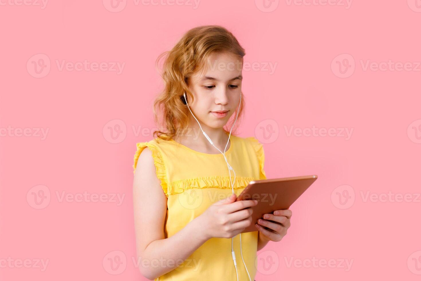 A teenage girl does her homework on a tablet. The student works and communicates with friends. Pink background with free space photo