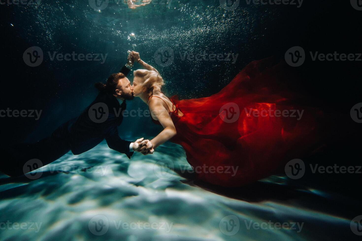 A woman in a red dress and a man in a suit are kissing underwater.A pair of floats under water photo