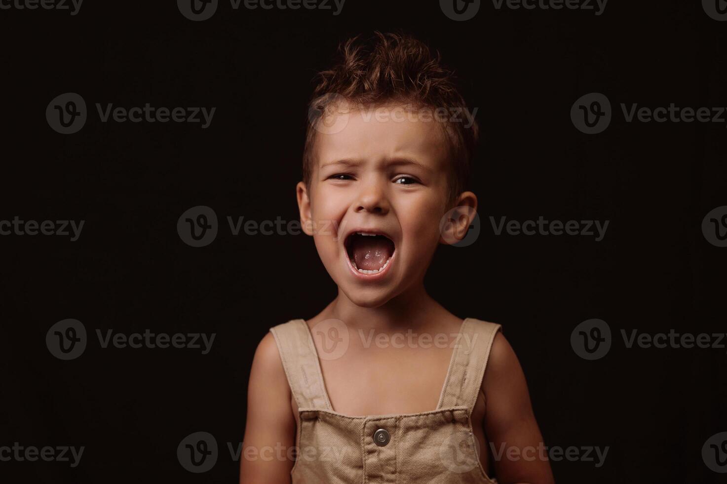 happy boy in overalls with stylish hairstyle screams photo