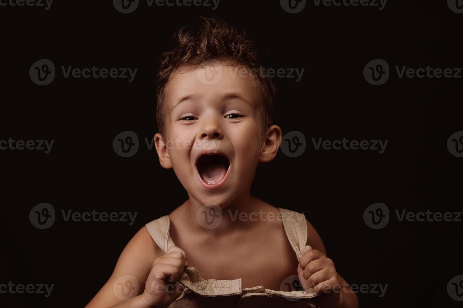 happy boy in overalls with stylish hairstyle screams photo