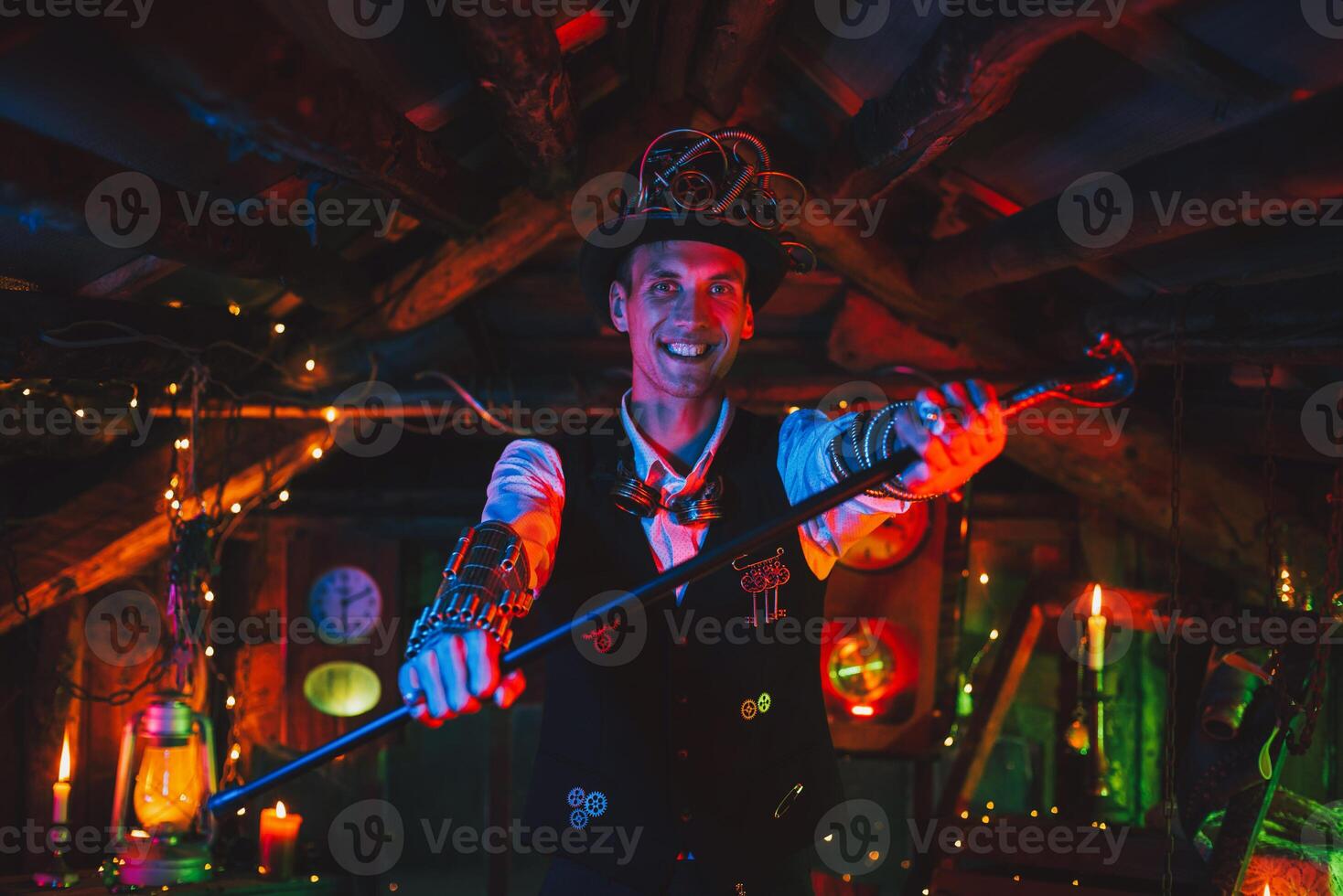 happy male inventor in a steampunk suit, top hat, glasses and with a cane smiles in a watch workshop photo