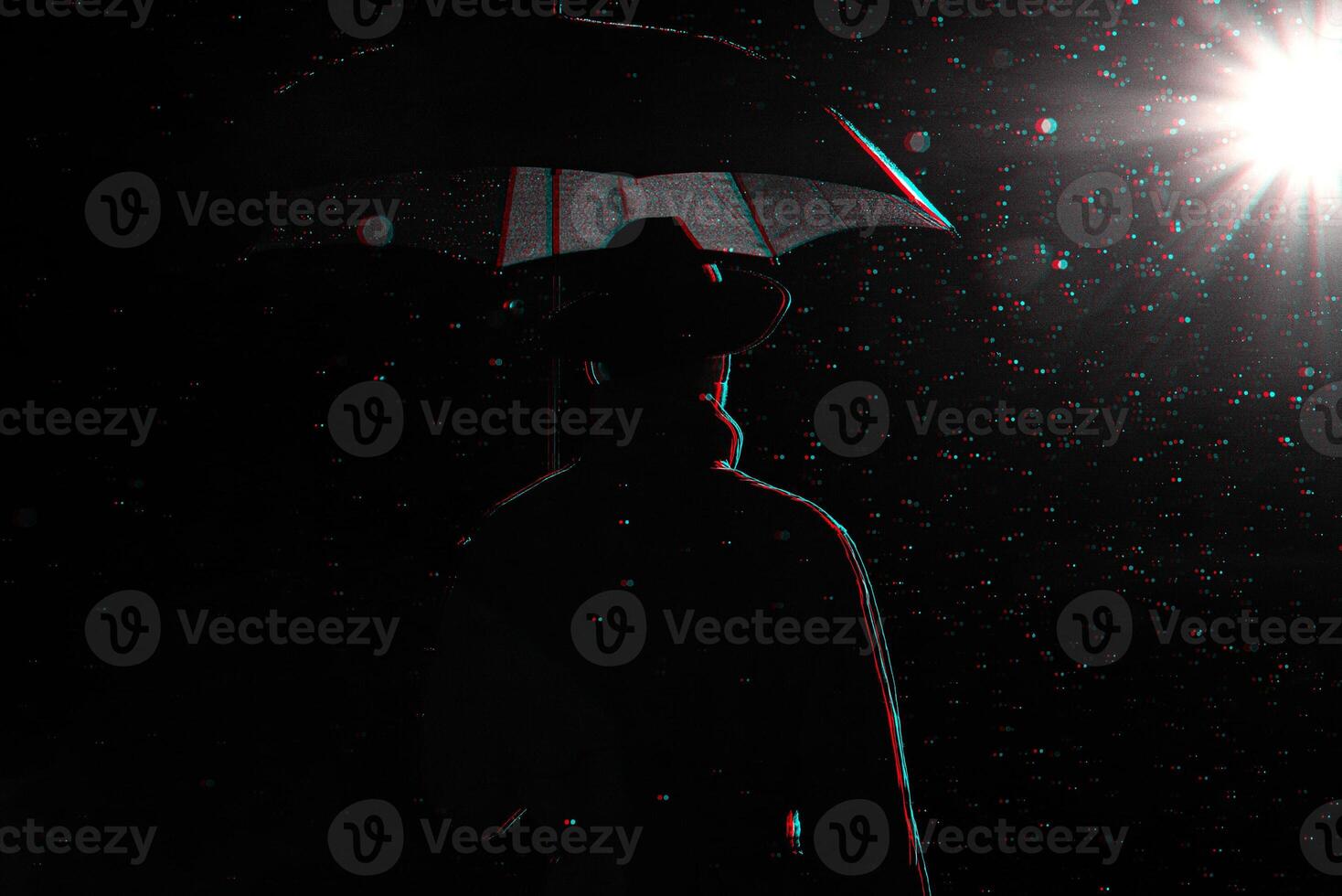 dark silhouette of a man in a raincoat and hat under an umbrella on the street in the rain photo