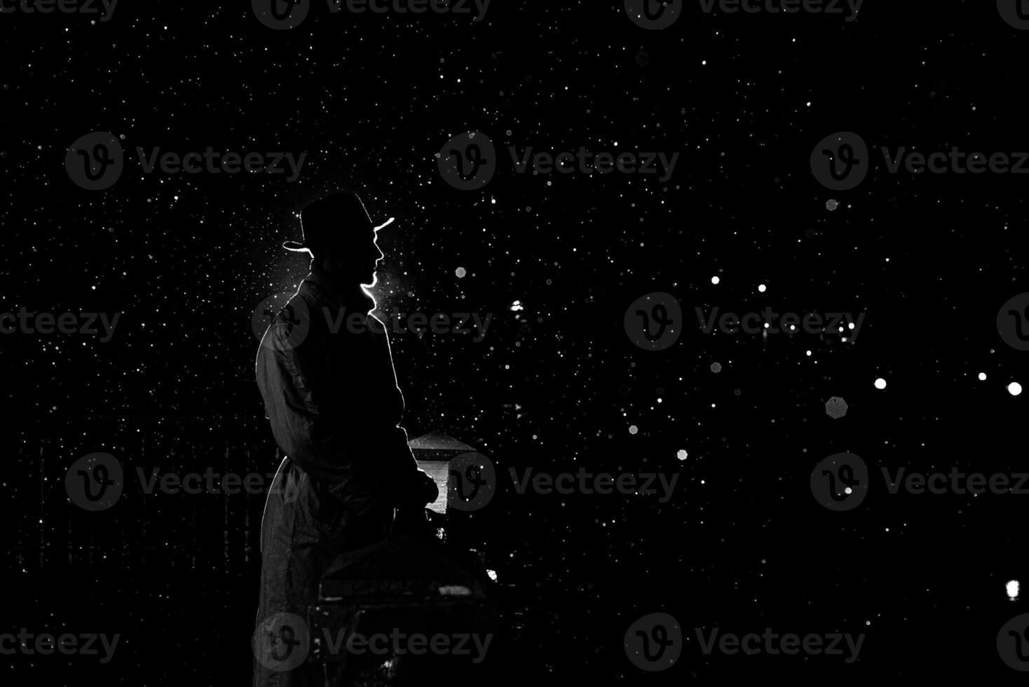 dark silhouette of a man in a hat at night in the rain in the city photo