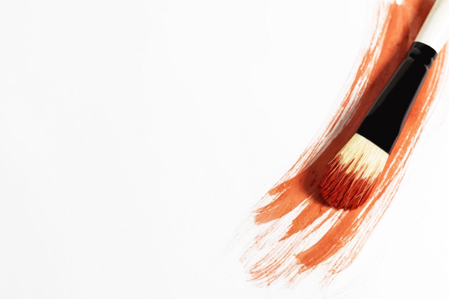 Red paint stroke on a white background with a brush to paint over it photo