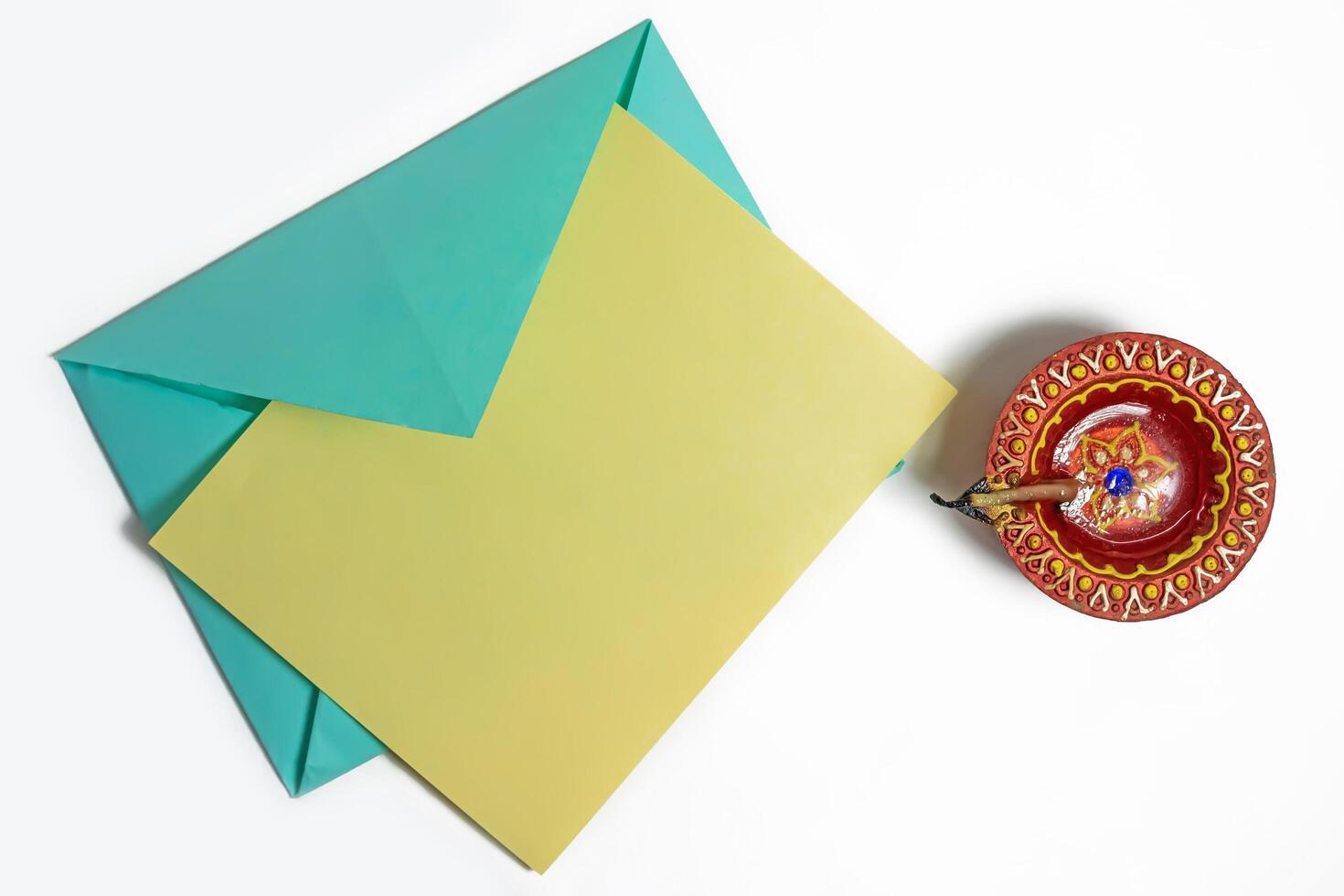 Vibrant envelope with blank note for festive greetings beside it traditional clay oil lamp on white background. photo