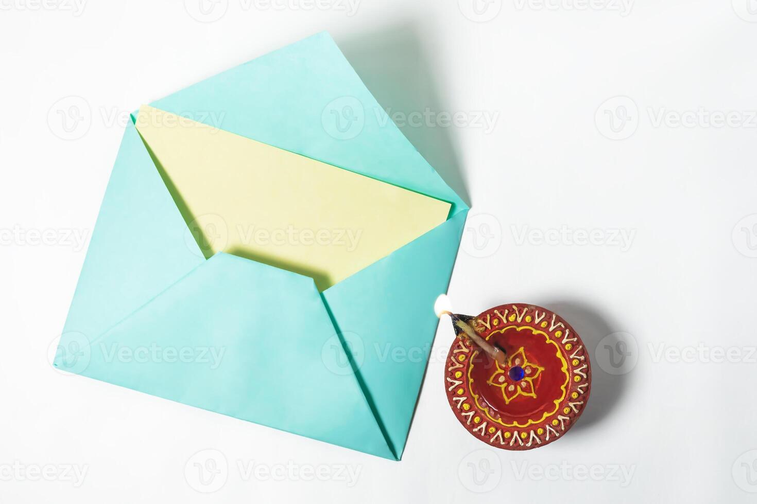Top view of illuminated Diwali diya with open greeting card envelope on white background. photo