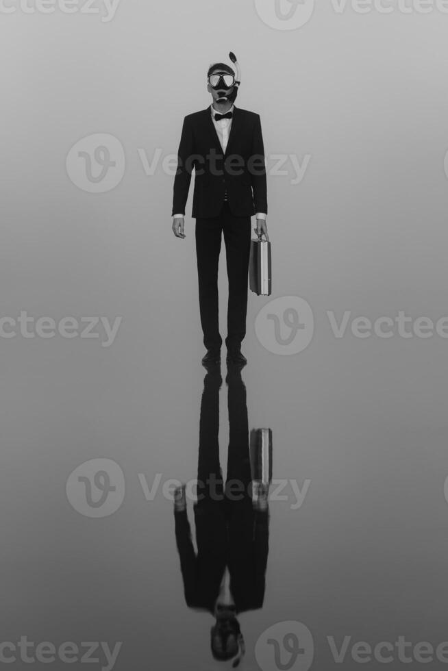 surreal portrait of a man in a suit and mask with a diving tube with a briefcase in his hands standing on the water photo