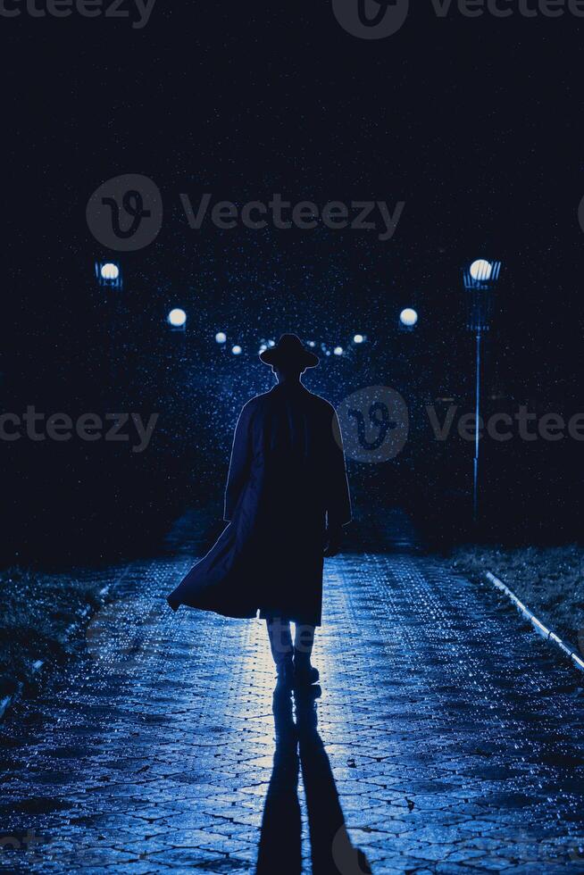 man detective agent in a hat and raincoat at night in a rainy city photo
