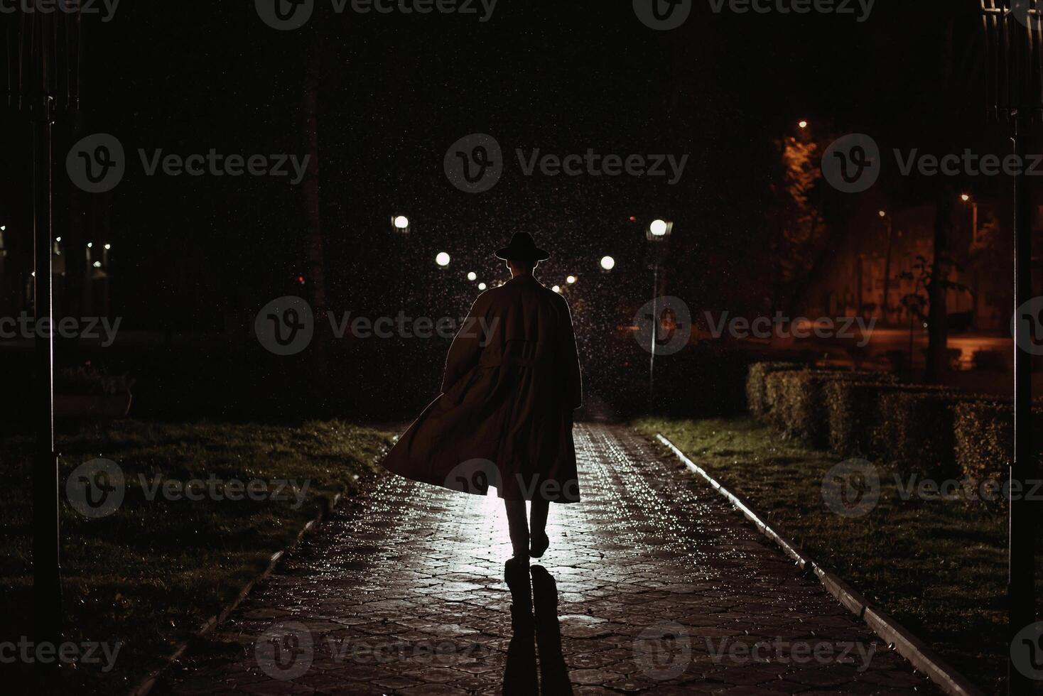 male detective in a hat and raincoat at night in a rainy city photo