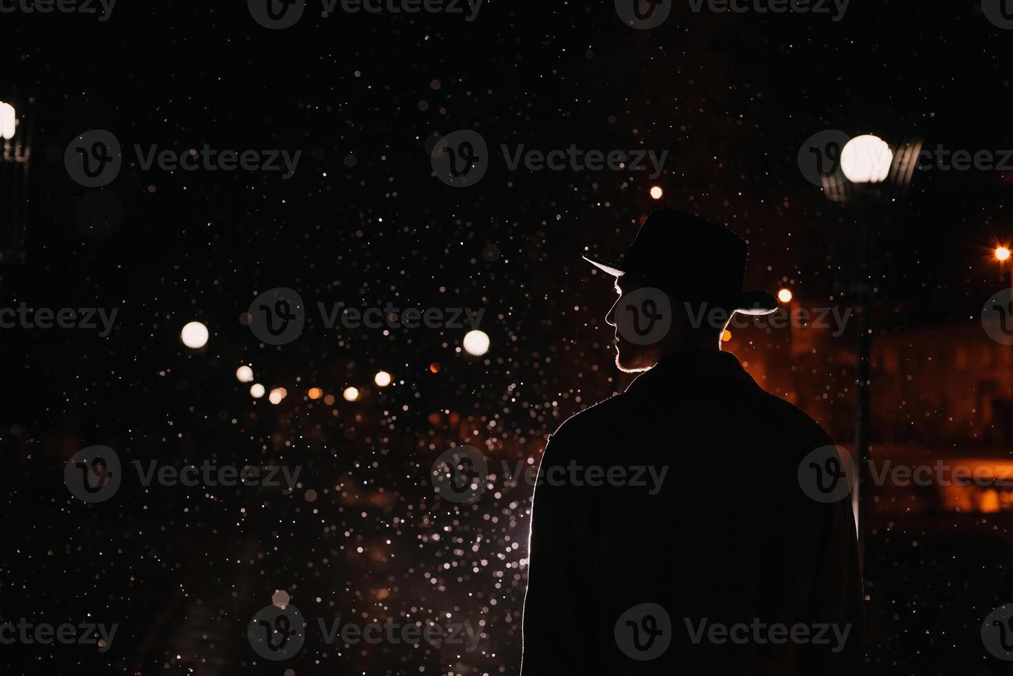 mafia man in a hat and raincoat at night in a rainy city photo