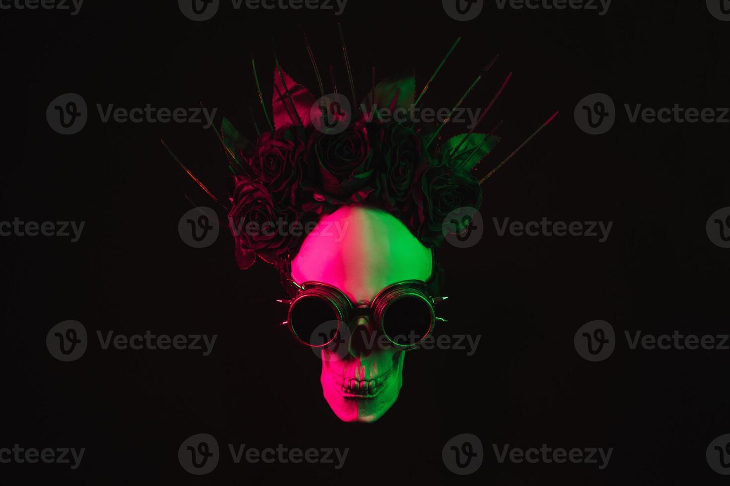human skull in steampunk glasses and a crown of flowers with pink green light photo