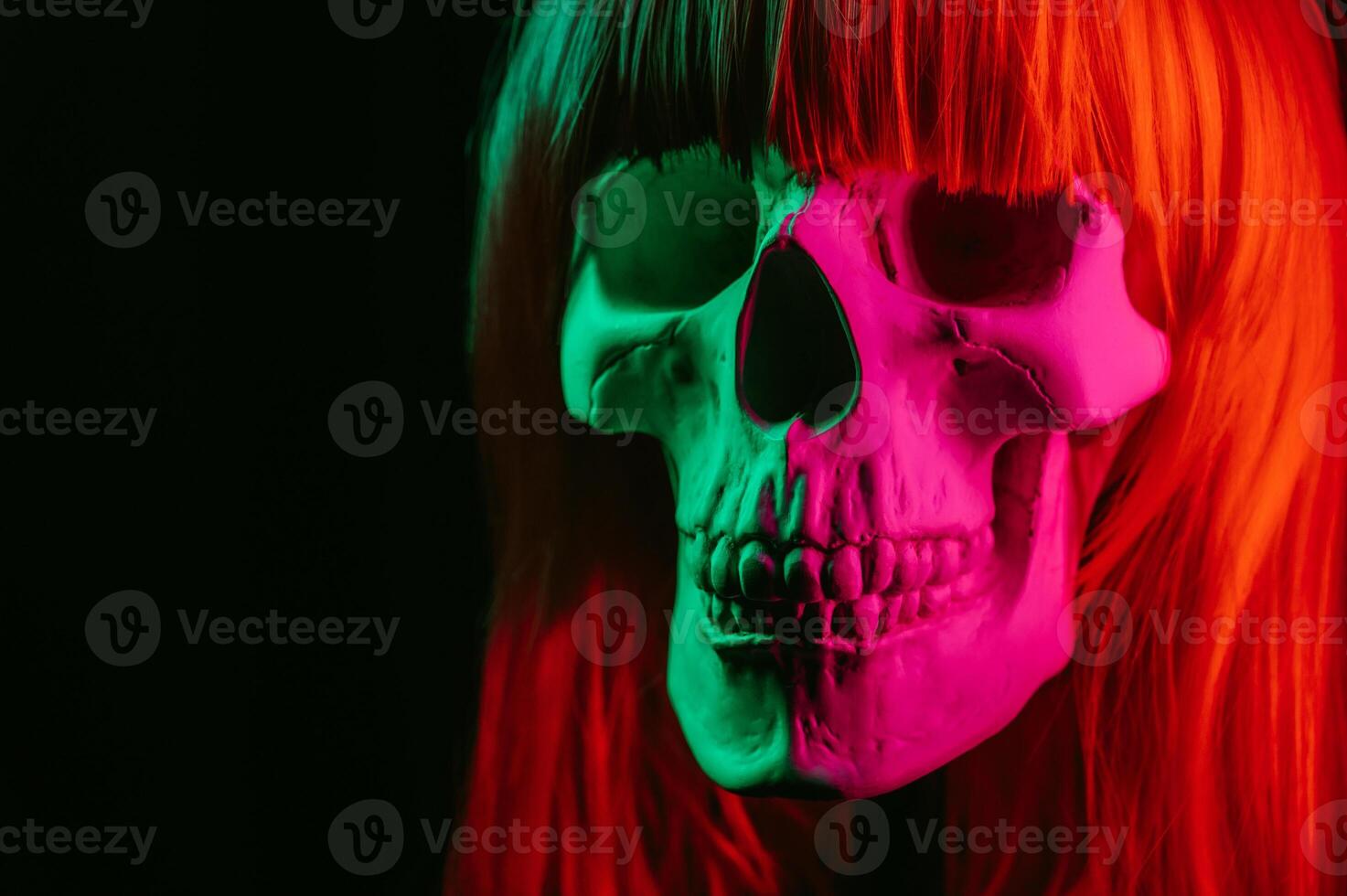 human skull of a woman in a wig with red hair with colored pink green light photo